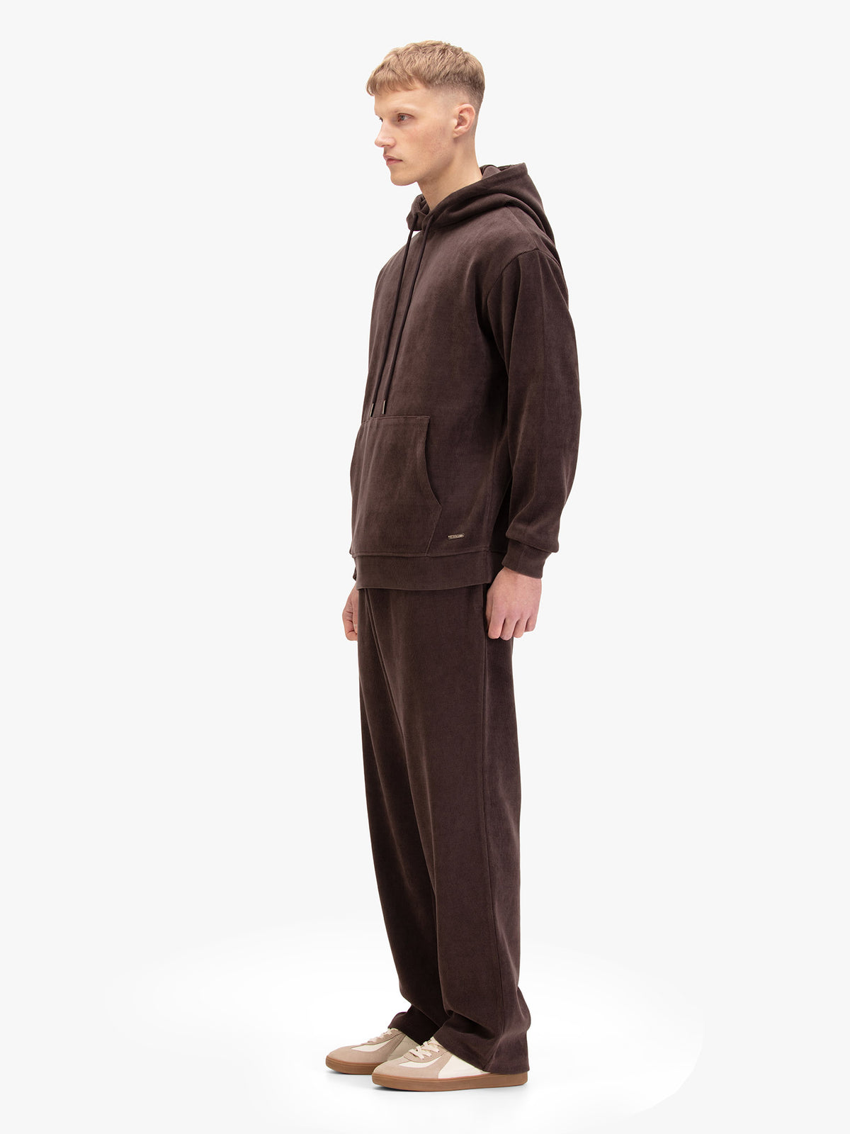 Men's relaxed-fit brown tracksuit with pullover hoodie and matching joggers, worn by a model, side view.