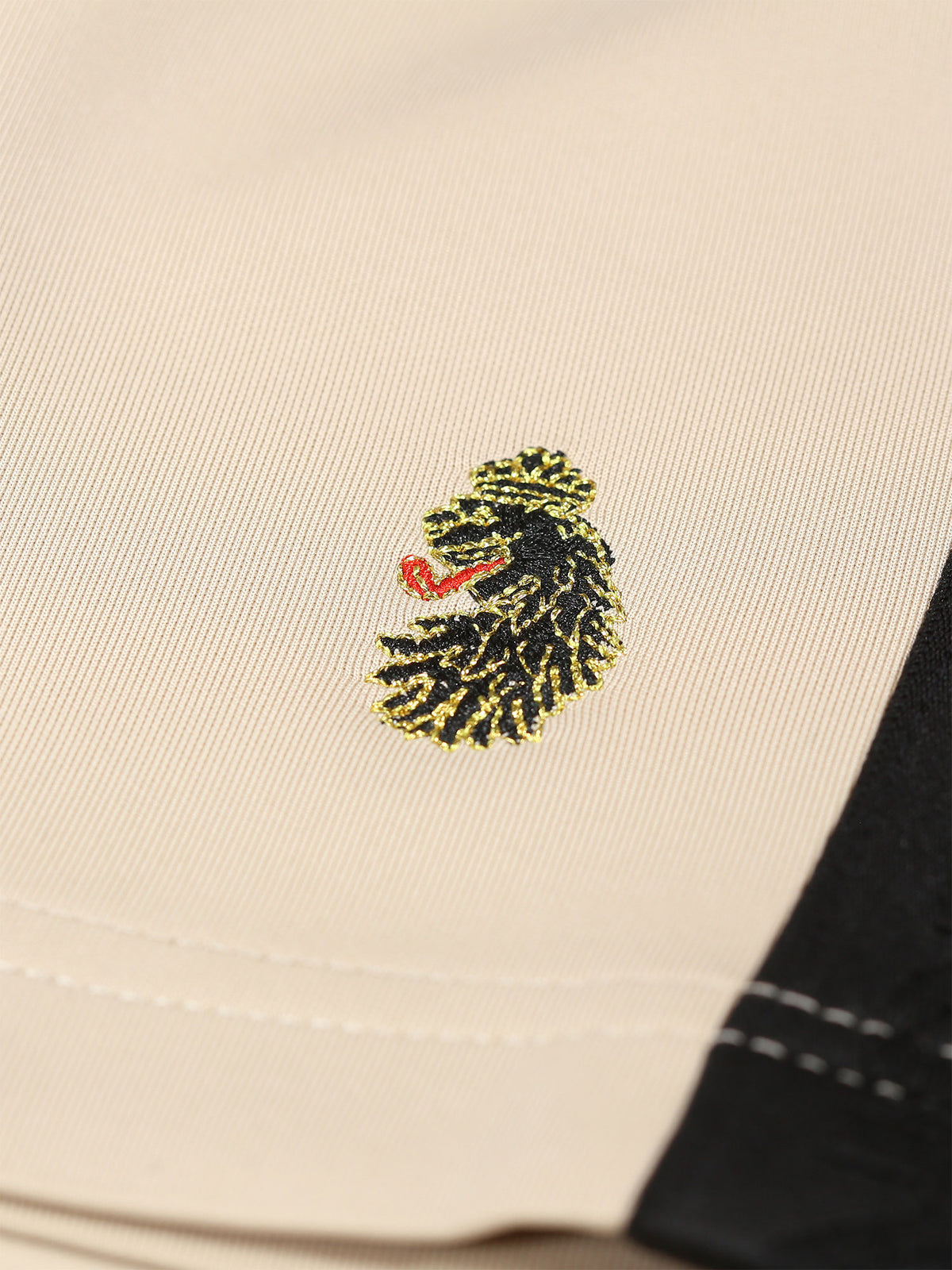 Close-up of LUKE lion head embroidery beside the contrast side tape on stone TTTST shorts