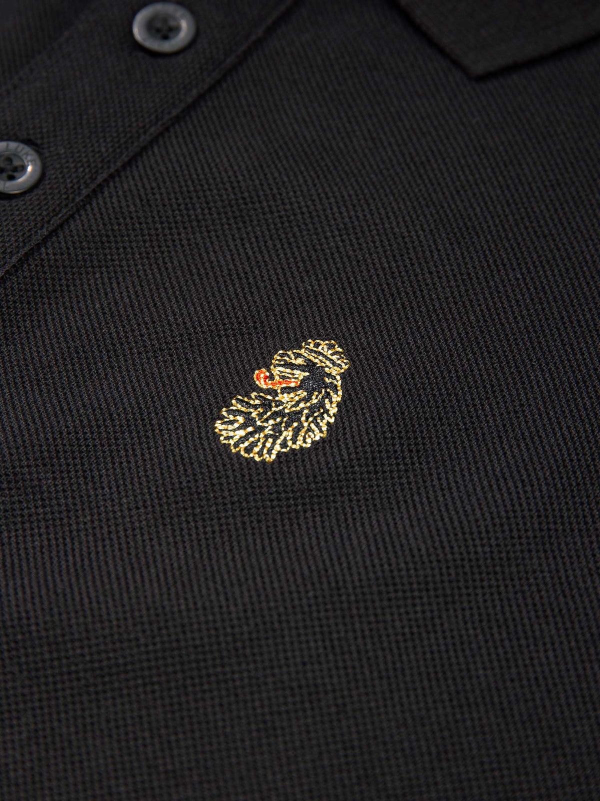 Close-up of gold LUKE lion head embroidery on black New Willtape polo shirt