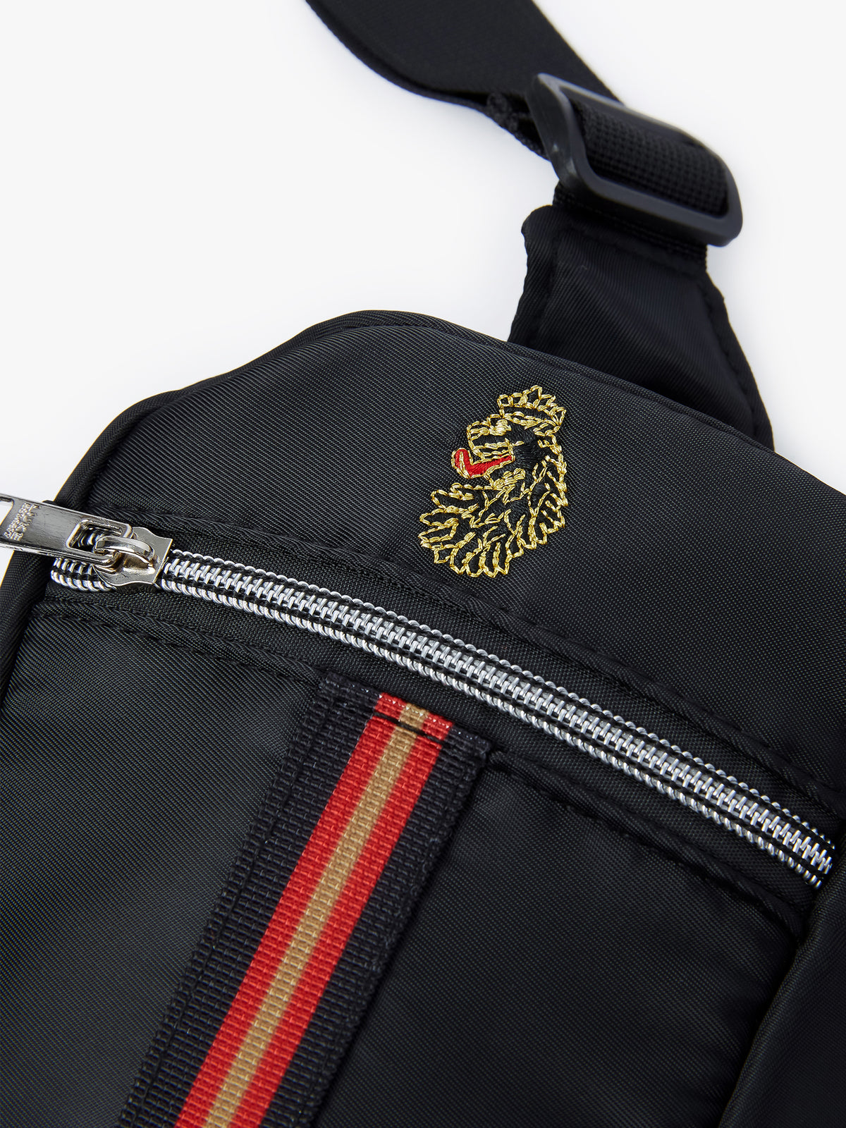 Close-up of LUKE lion head embroidery and tri-colour trim tape on black Euston cross body bag