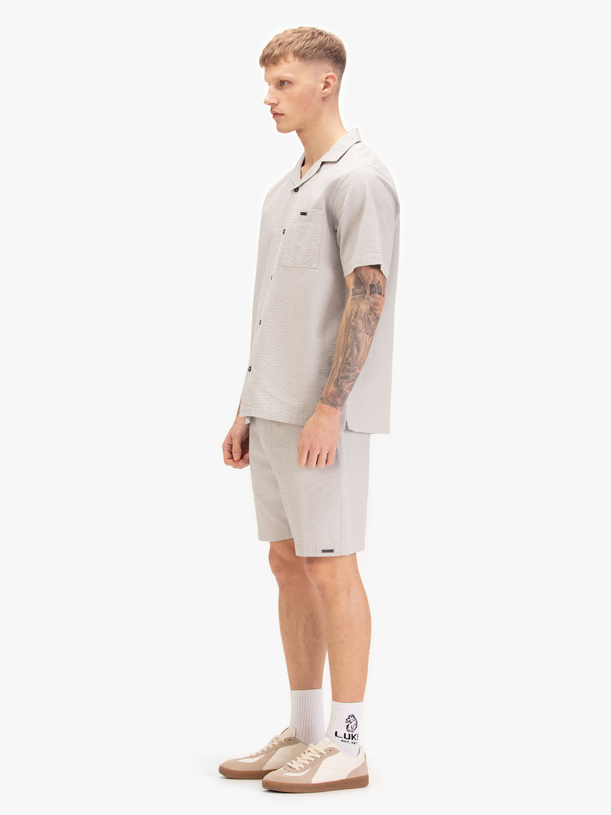 Men's grey short set with short-sleeve button-up shirt and matching shorts, worn by a model, side view.