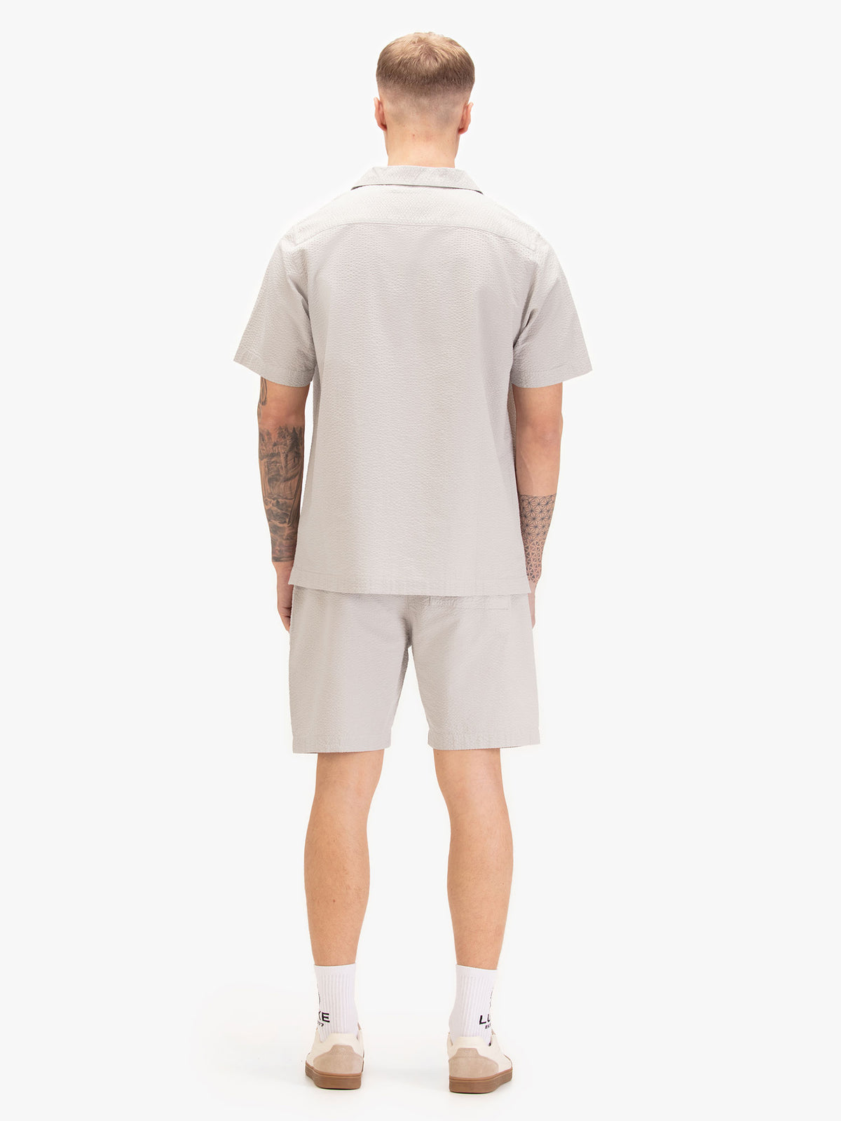 Men's grey short set with short-sleeve button-up shirt and matching shorts, worn by a model, back view.