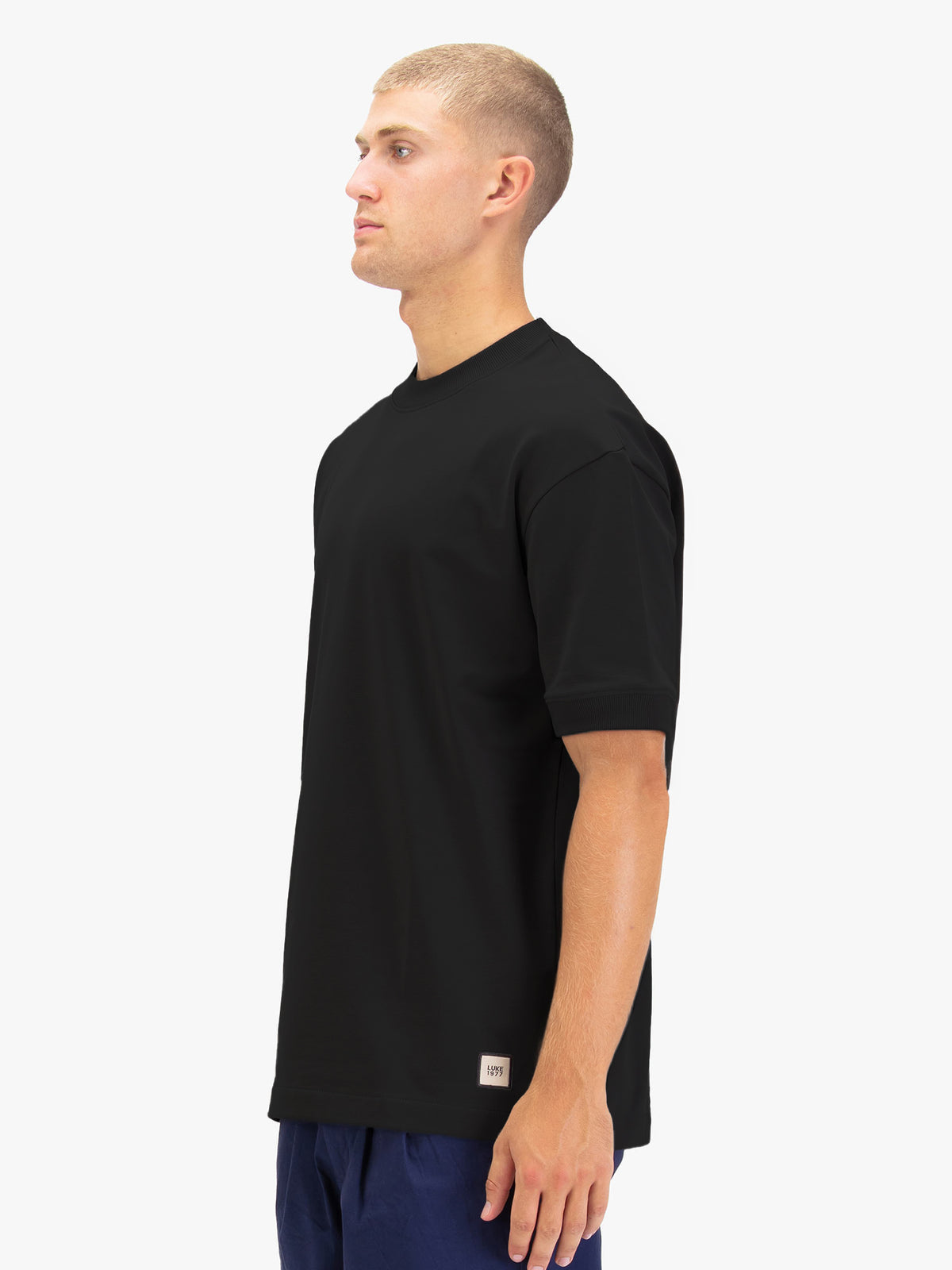 Men's black t-shirt with crew neck and short sleeves worn by a model - side view.