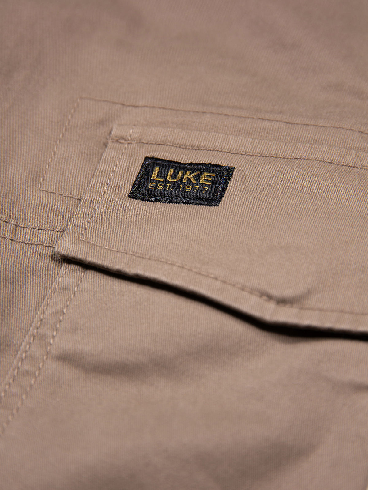 Close-up of LUKE EST. 1977 woven badge on leg pocket of Hardnut brown Panama cargo trousers