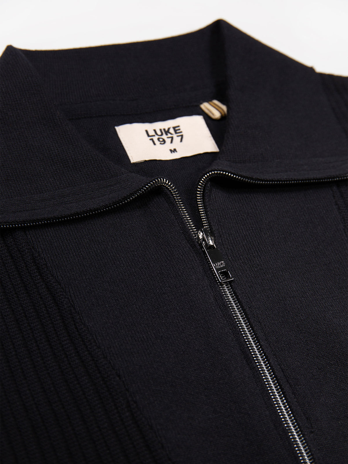 Close-up of rib funnel neck, zip and LUKE 1977 neck label on black Lifton knit