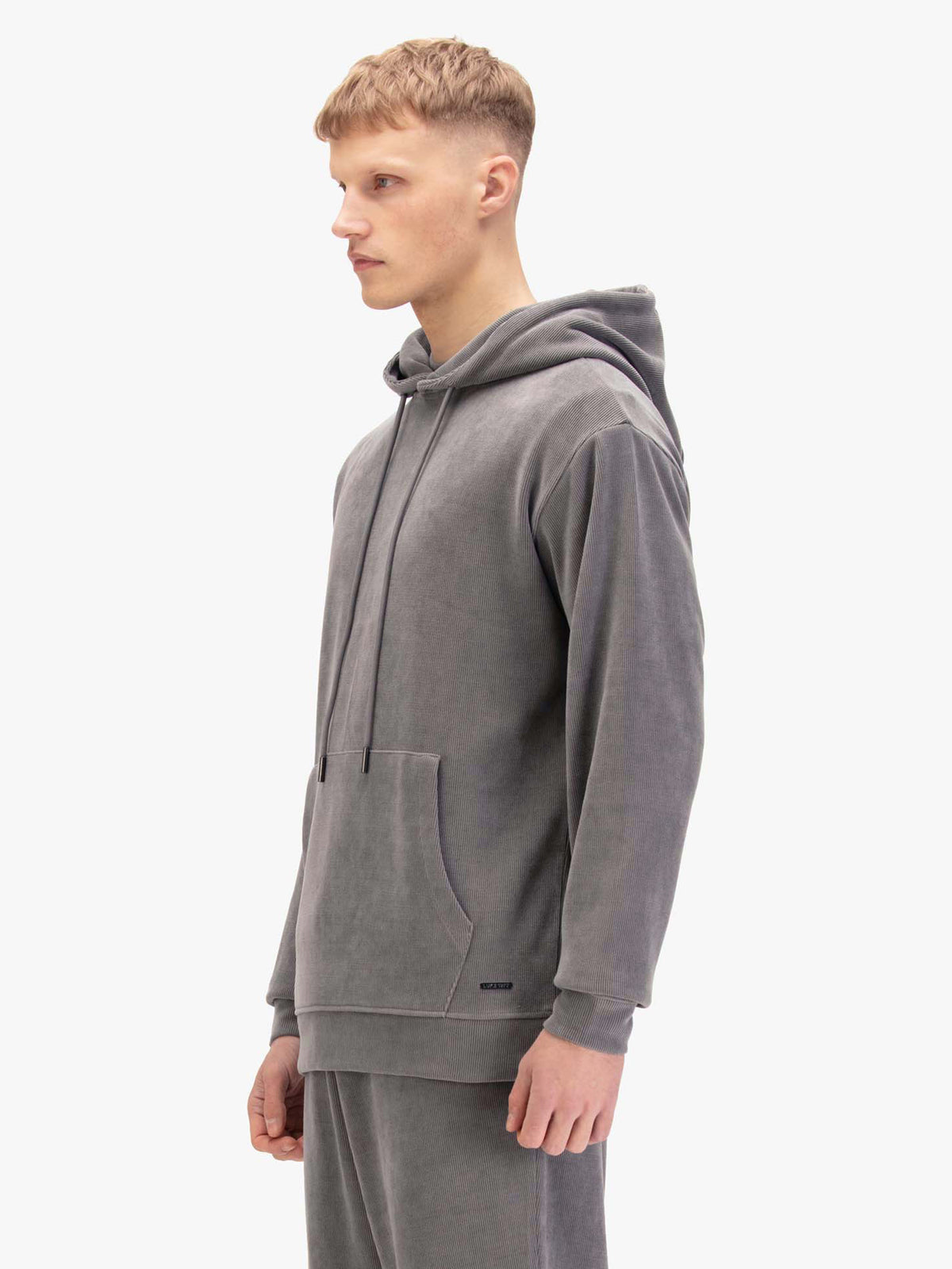 Men's relaxed-fit grey hoodie with front pocket and drawstring hood, worn by a model, side view