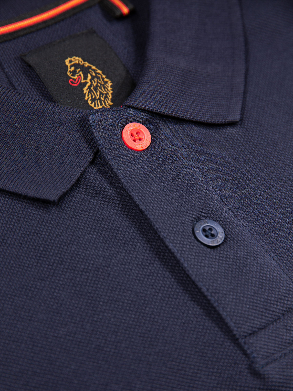 Close-up of marina red top button, smoke button and lion embroidery on navy New Mead polo shirt