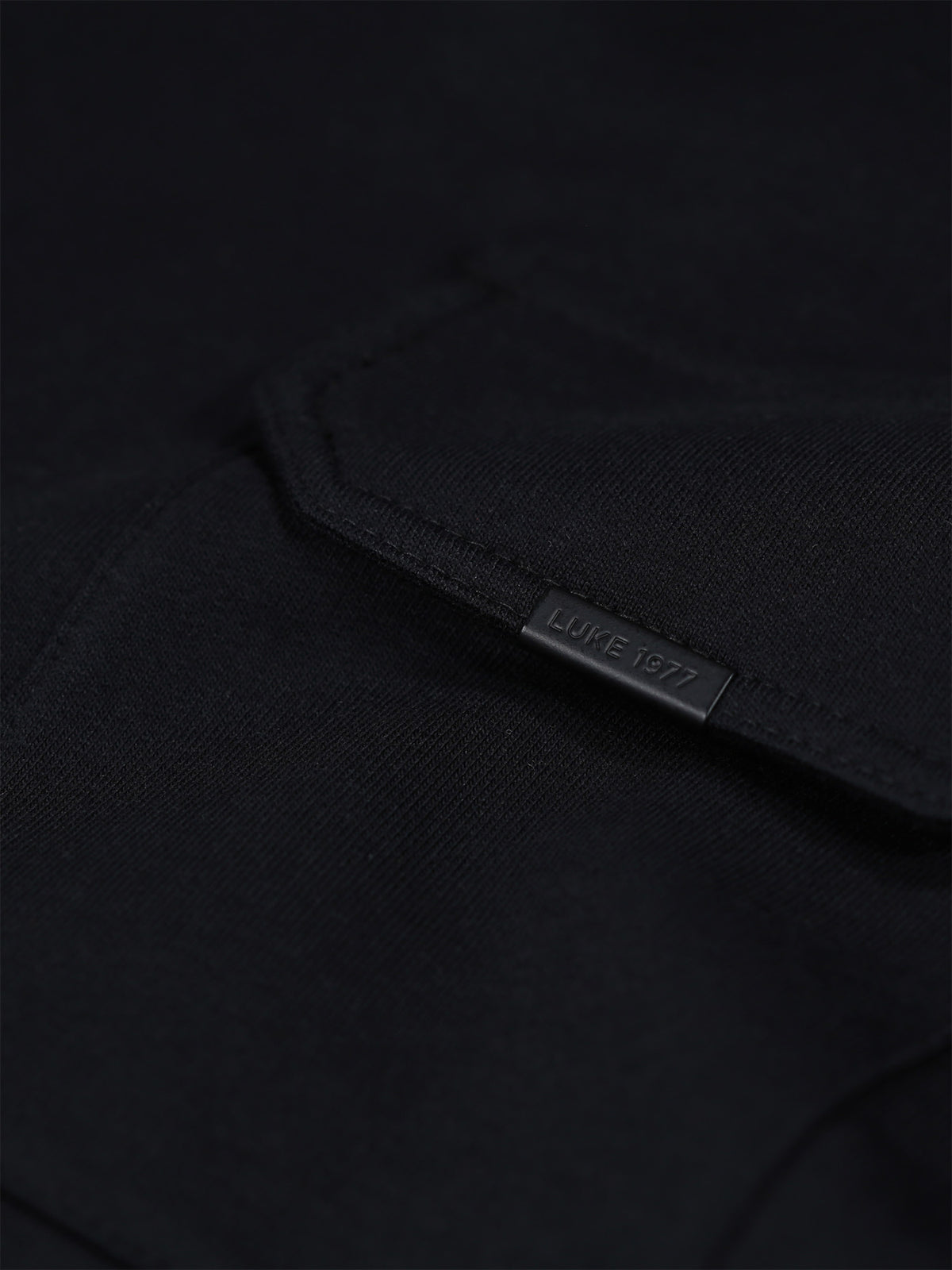Close-up of chest pocket with LUKE 1977 text branded metal clip on black Dragger t-shirt