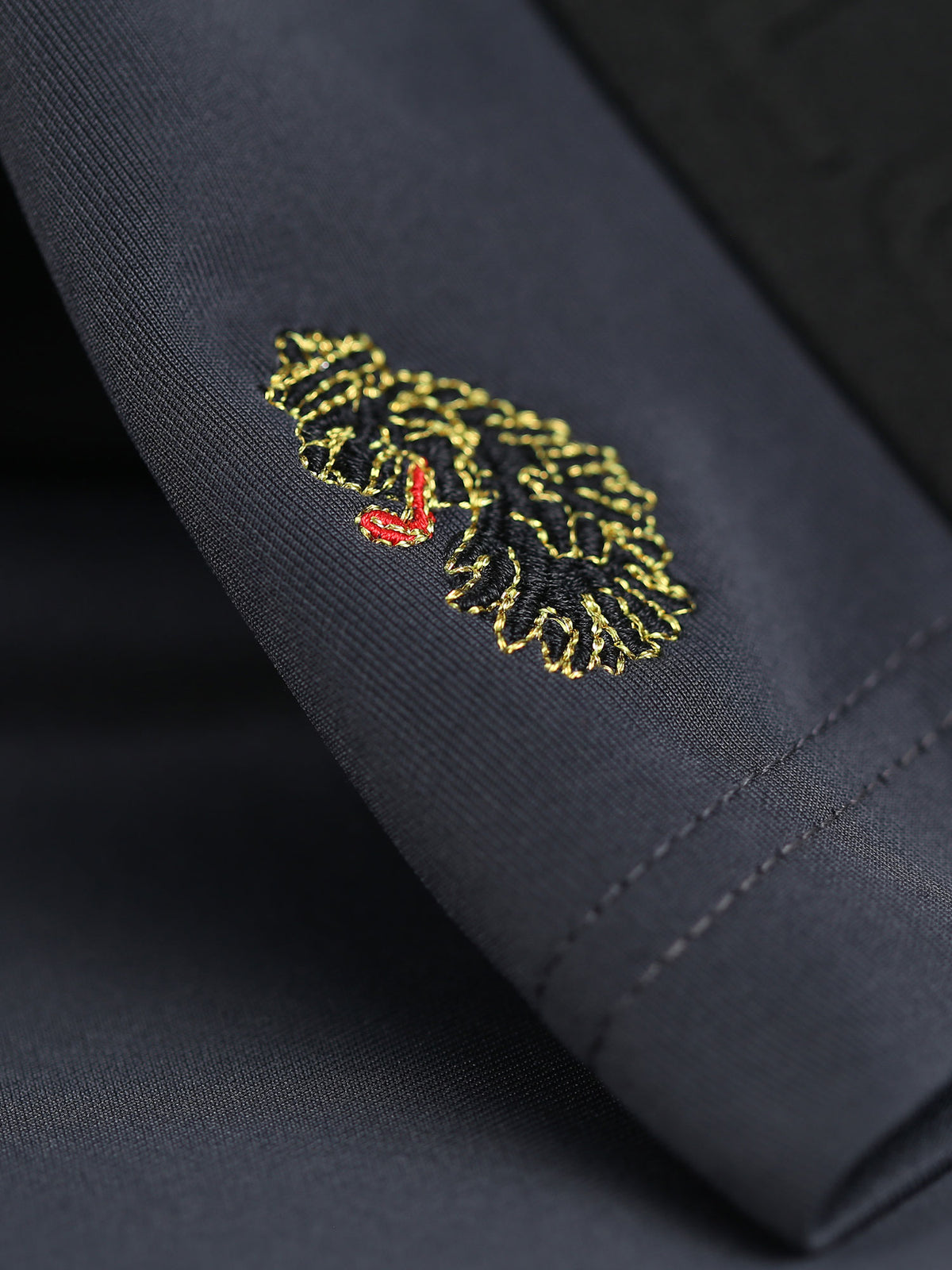 Close-up of gold LUKE 1977 lion head embroidery at the hem of charcoal TTTST shorts
