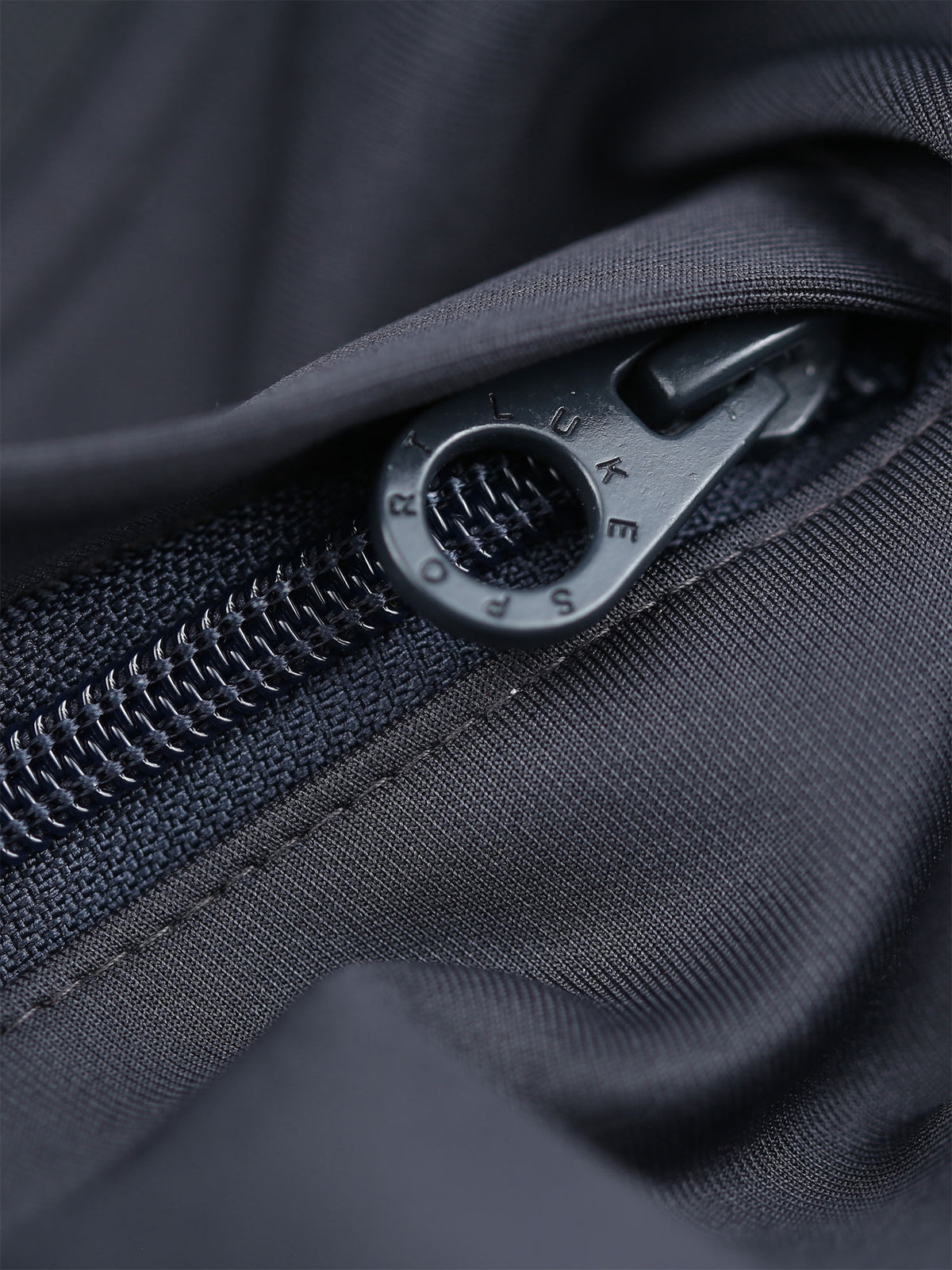 Close-up of branded tonal metal zip puller on charcoal TTTST tricot shorts