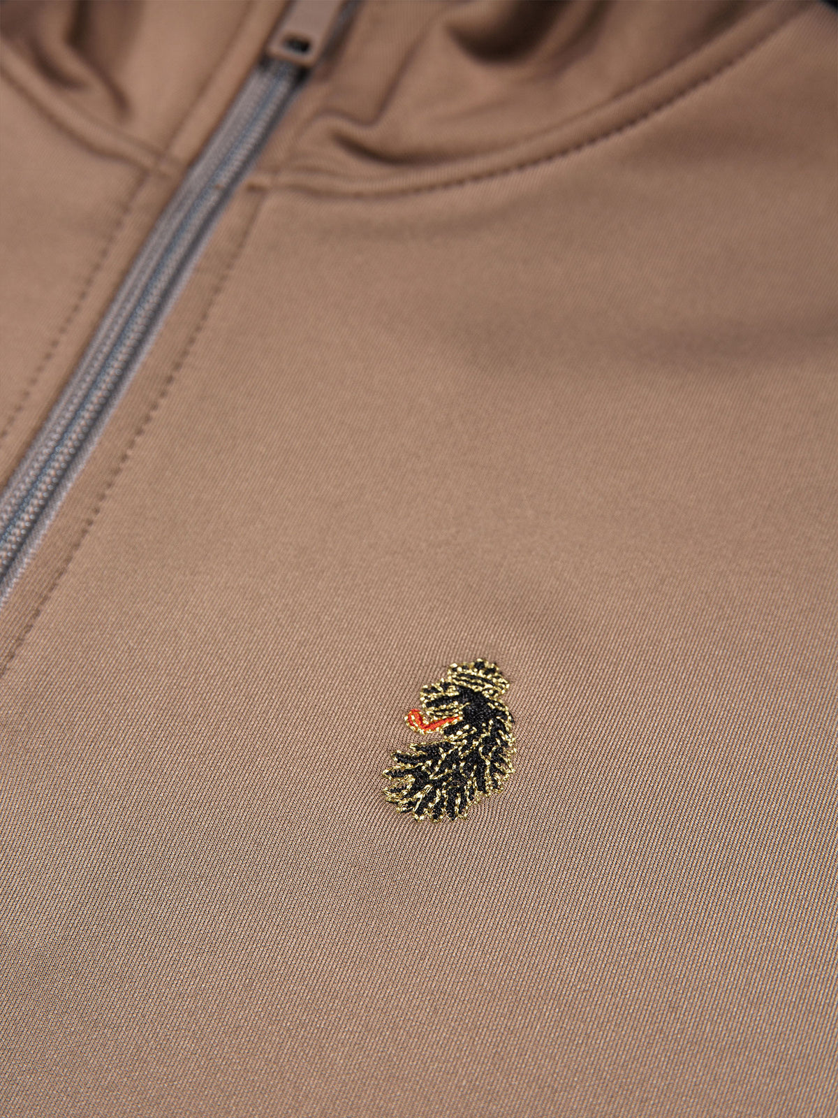 Close-up of gold LUKE lion head embroidery on brown TTTQR sweatshirt