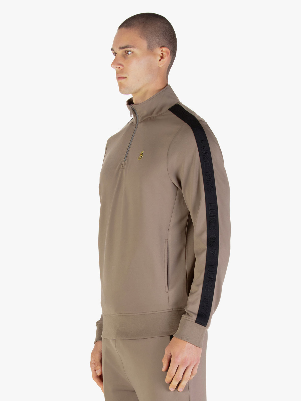 Side view of man wearing brown LUKE 1977 TTTQR tricot sweatshirt showing contrast sleeve tape