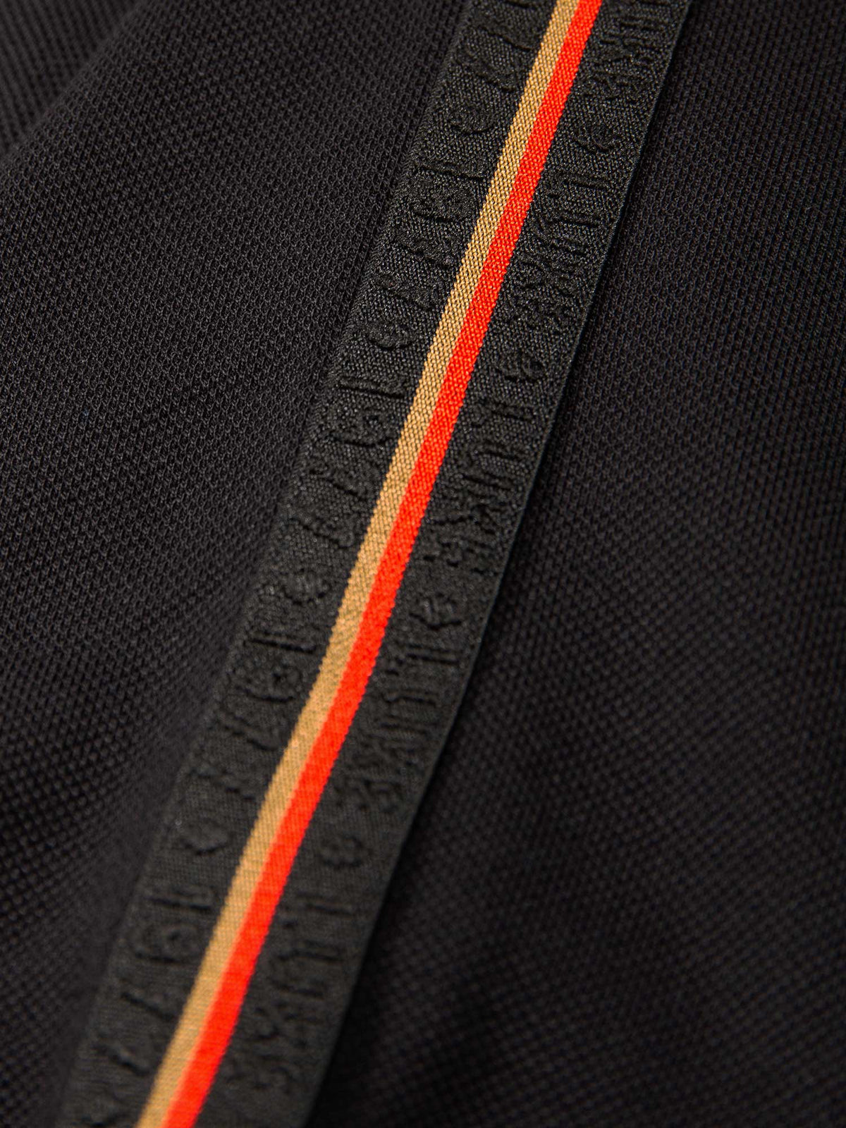 Close-up of LUKE 1977 raised text elasticated jacquard tape on black Willtape polo
