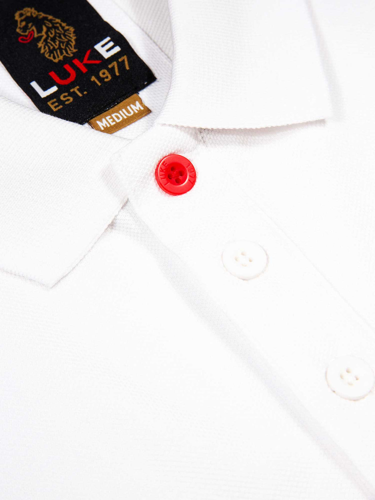 Close-up of rib collar, red top button and neck label on white New Willtape polo shirt