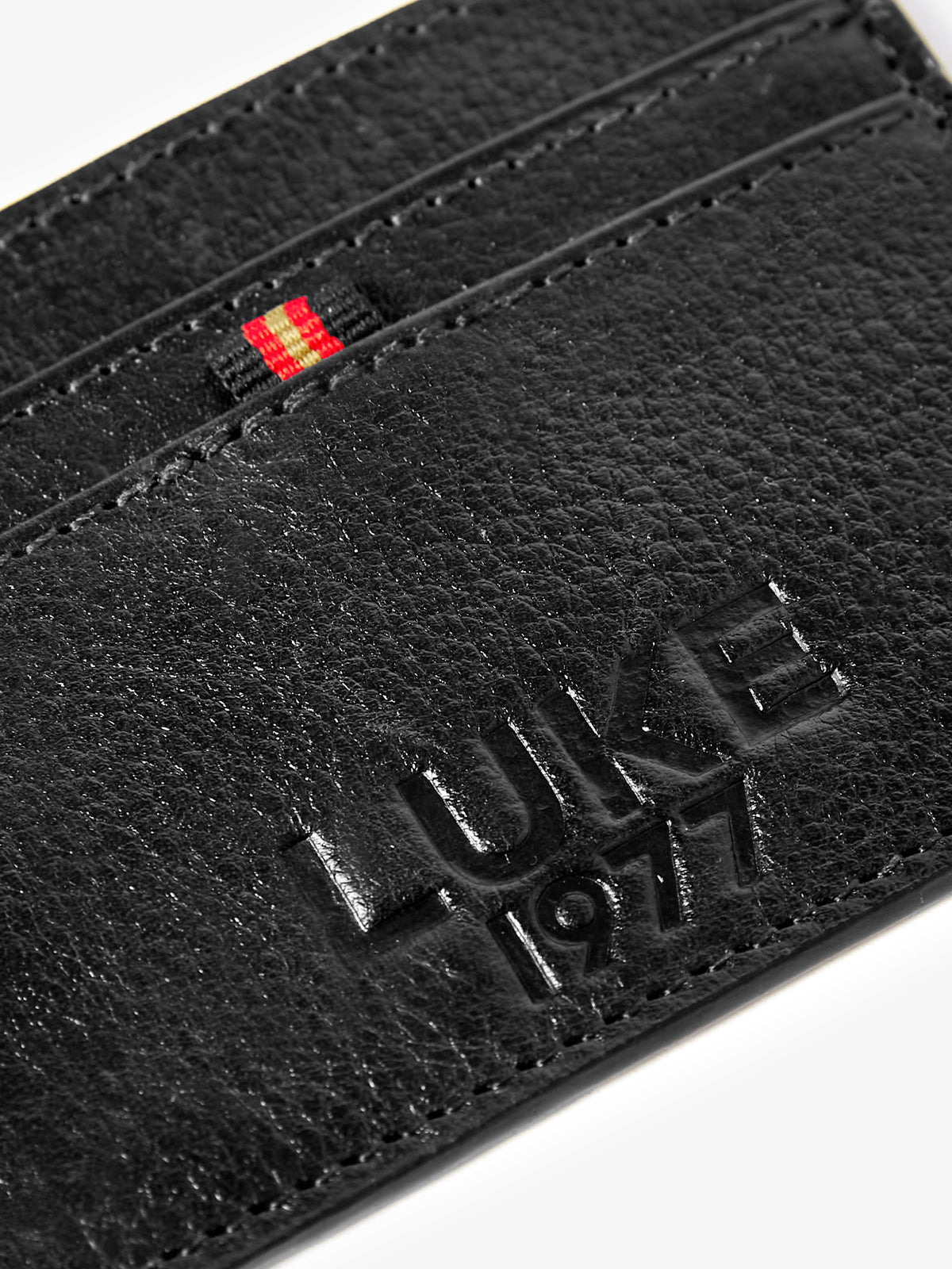 Close-up of debossed LUKE 1977 text and tri-colour trim tape on black Milled card holder