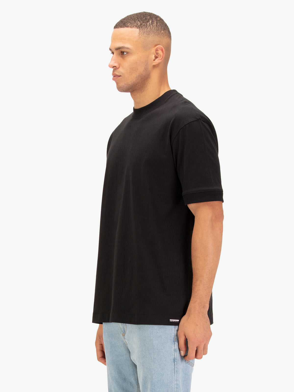 Men's black t-shirt with crew neck and short sleeves worn by a model - side view.