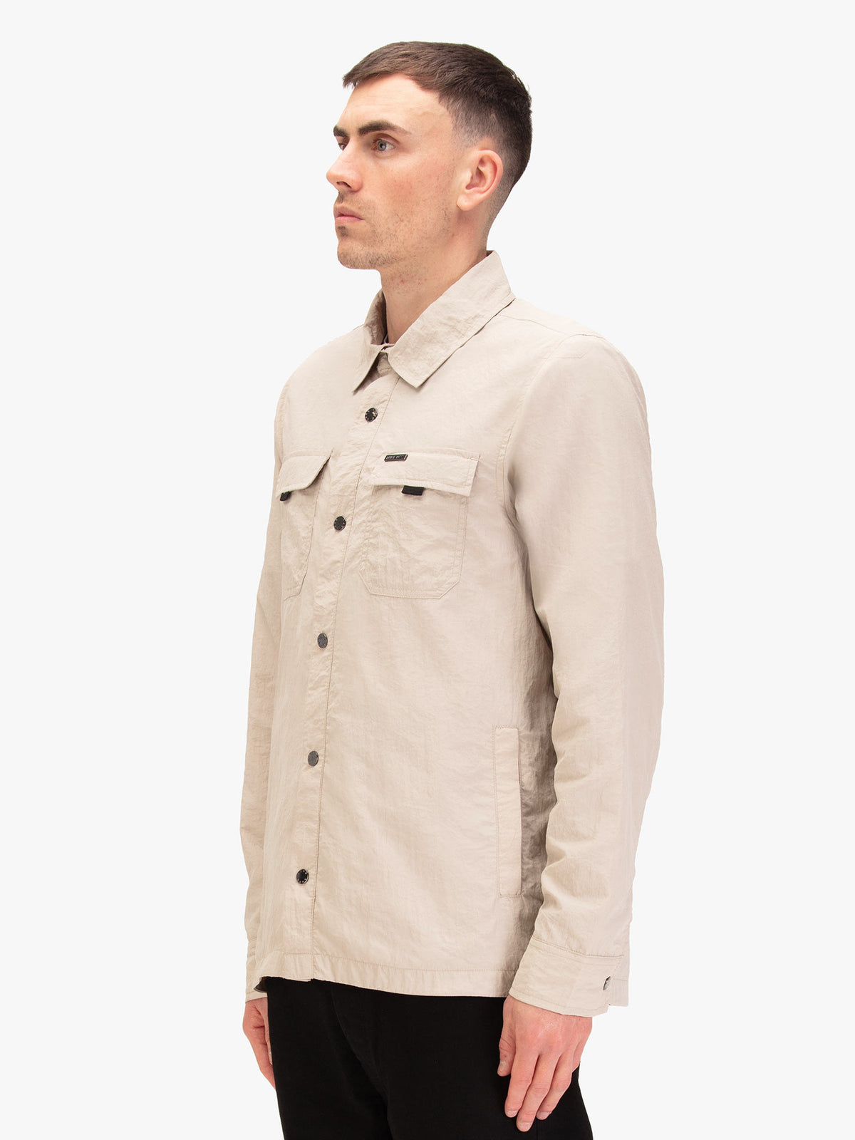 Men's beige jacket with button-up front and chest pocket, worn by a model, side view