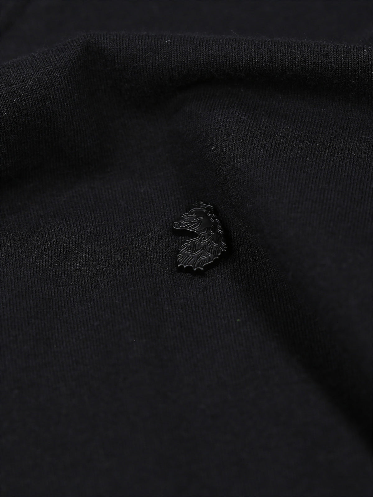 Close-up of subtle metal lion head rivet on chest of black Shanghai Modal t-shirt