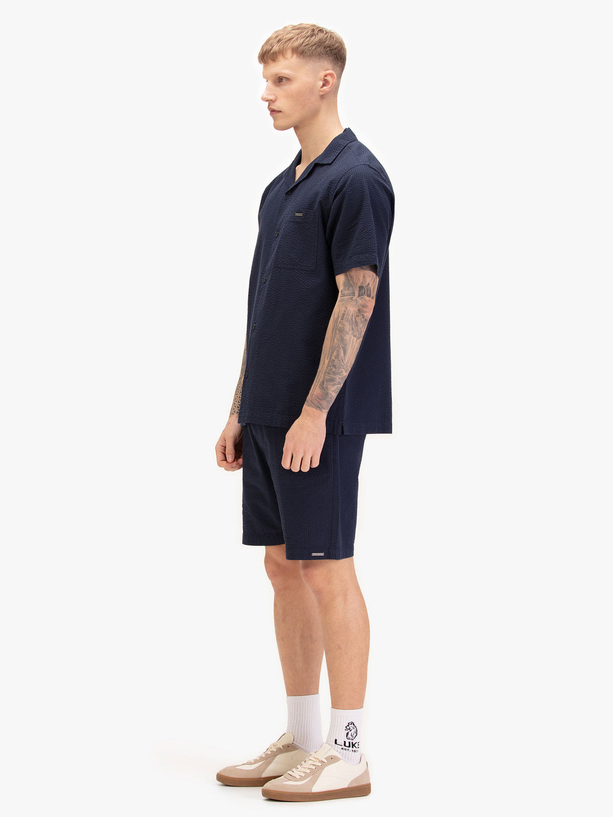 Men's navy short set with short-sleeve button-up shirt and matching shorts, worn by a model, side view.
