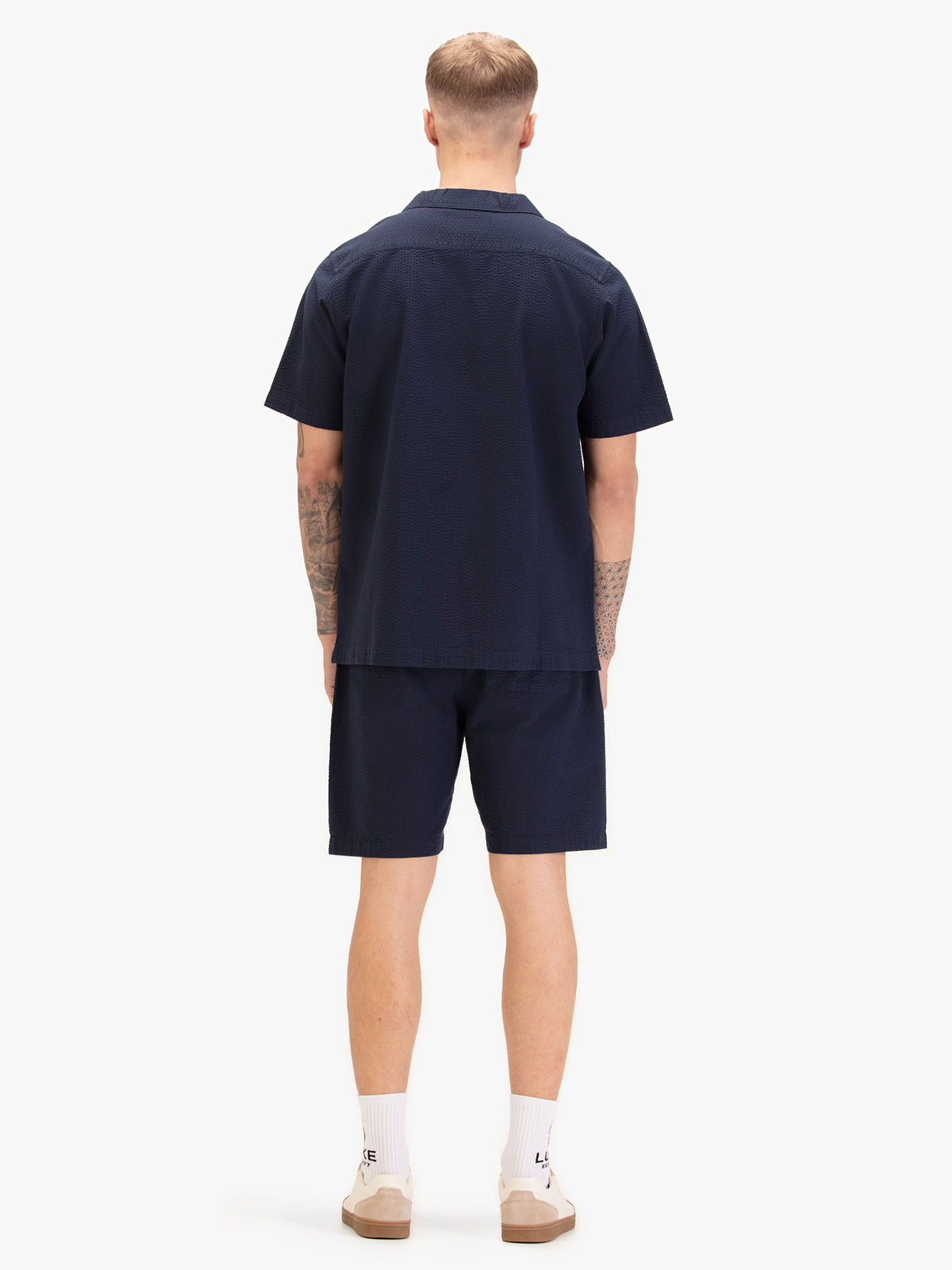 Men's navy short set with short-sleeve button-up shirt and matching shorts, worn by a model, back view.