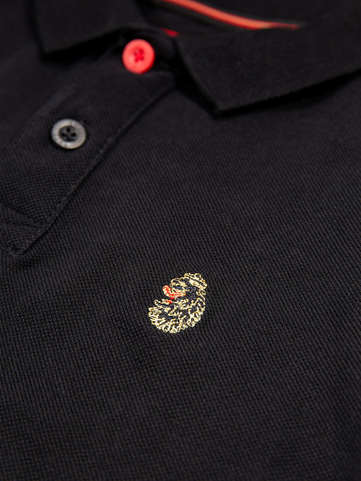 Close-up of LUKE lion embroidery on black Williams 1000 junior polo shirt