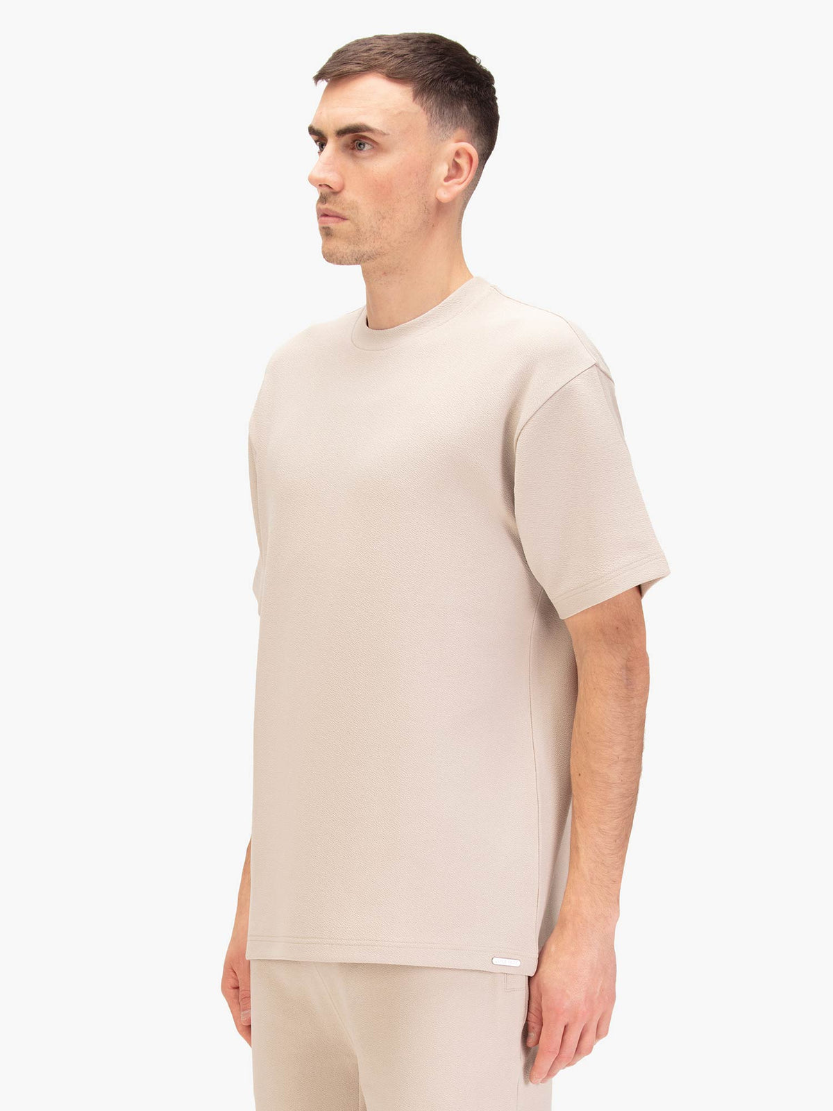Men's relaxed-fit beige t-shirt with crew neck and short sleeves, worn by a model, side view