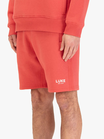 Men's red shorts with drawstring waistband, worn by a model, side view