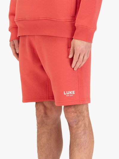 Men's red shorts with drawstring waistband, worn by a model, side view