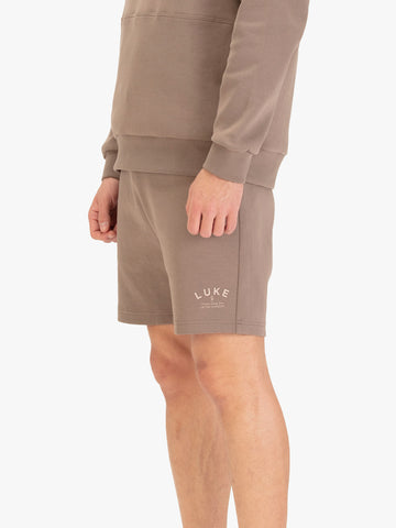 Men's brown shorts with drawstring waistband, worn by a model, side view