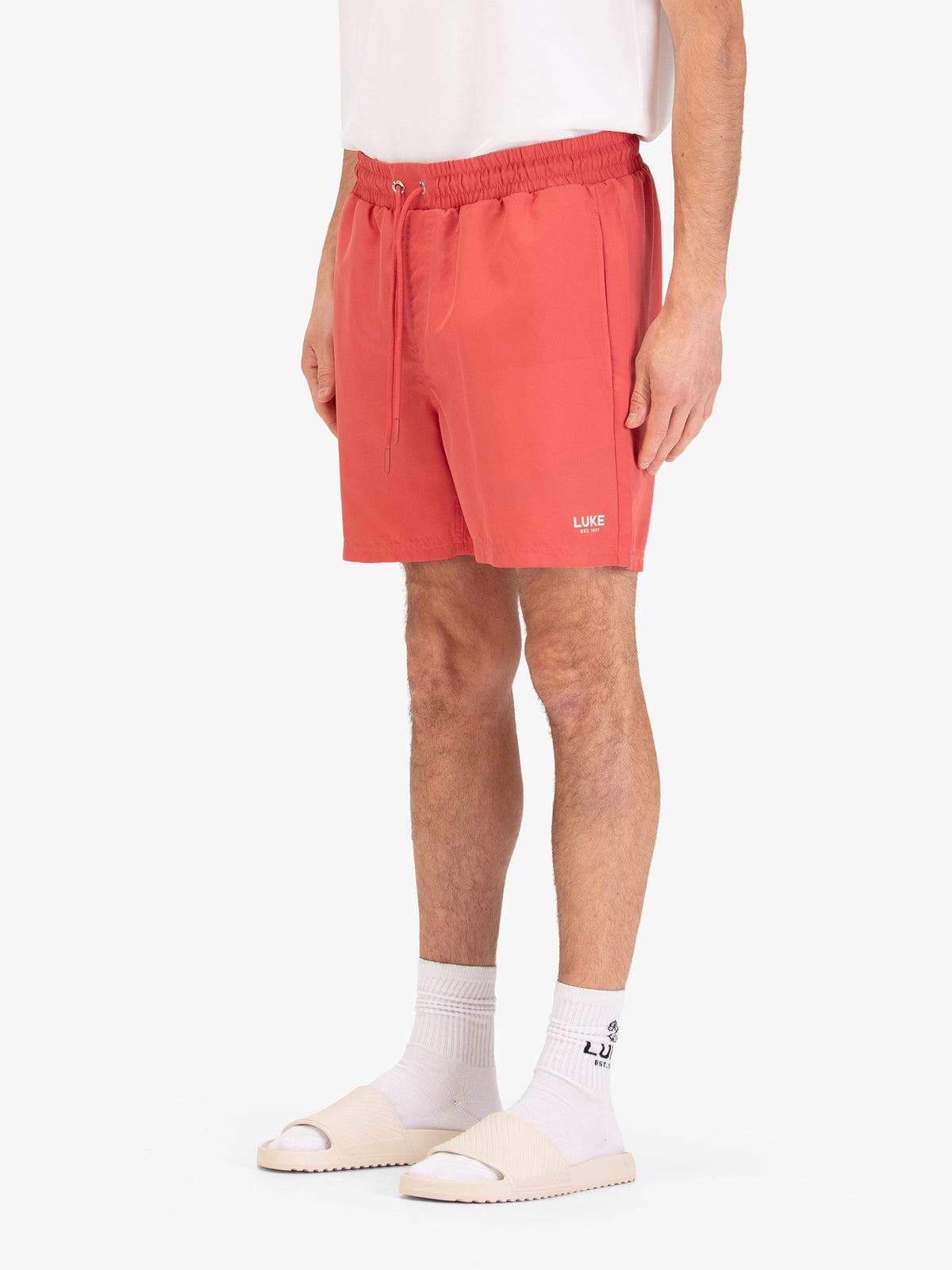 Men's red swim shorts with drawstring waistband, worn by a model, side view