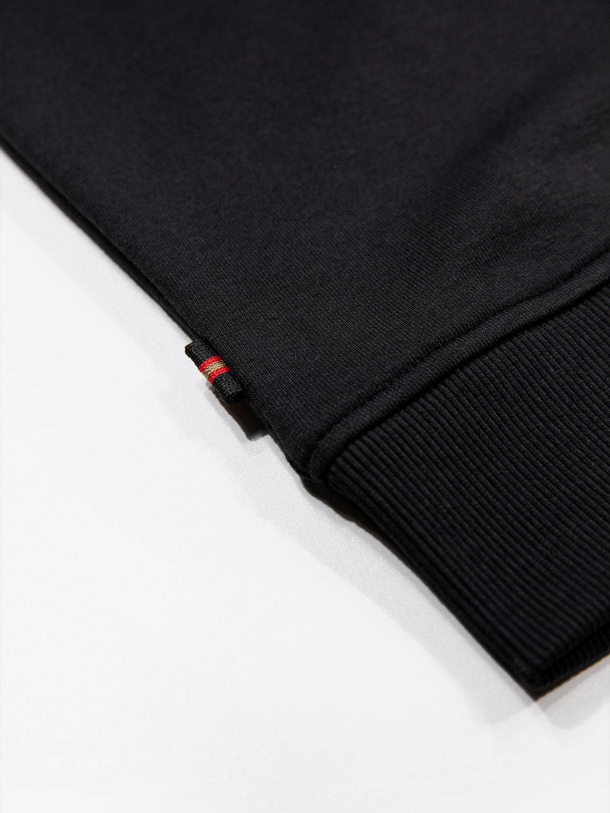 Close-up of rib hem and small red tab on black Jan Jose sweatshirt
