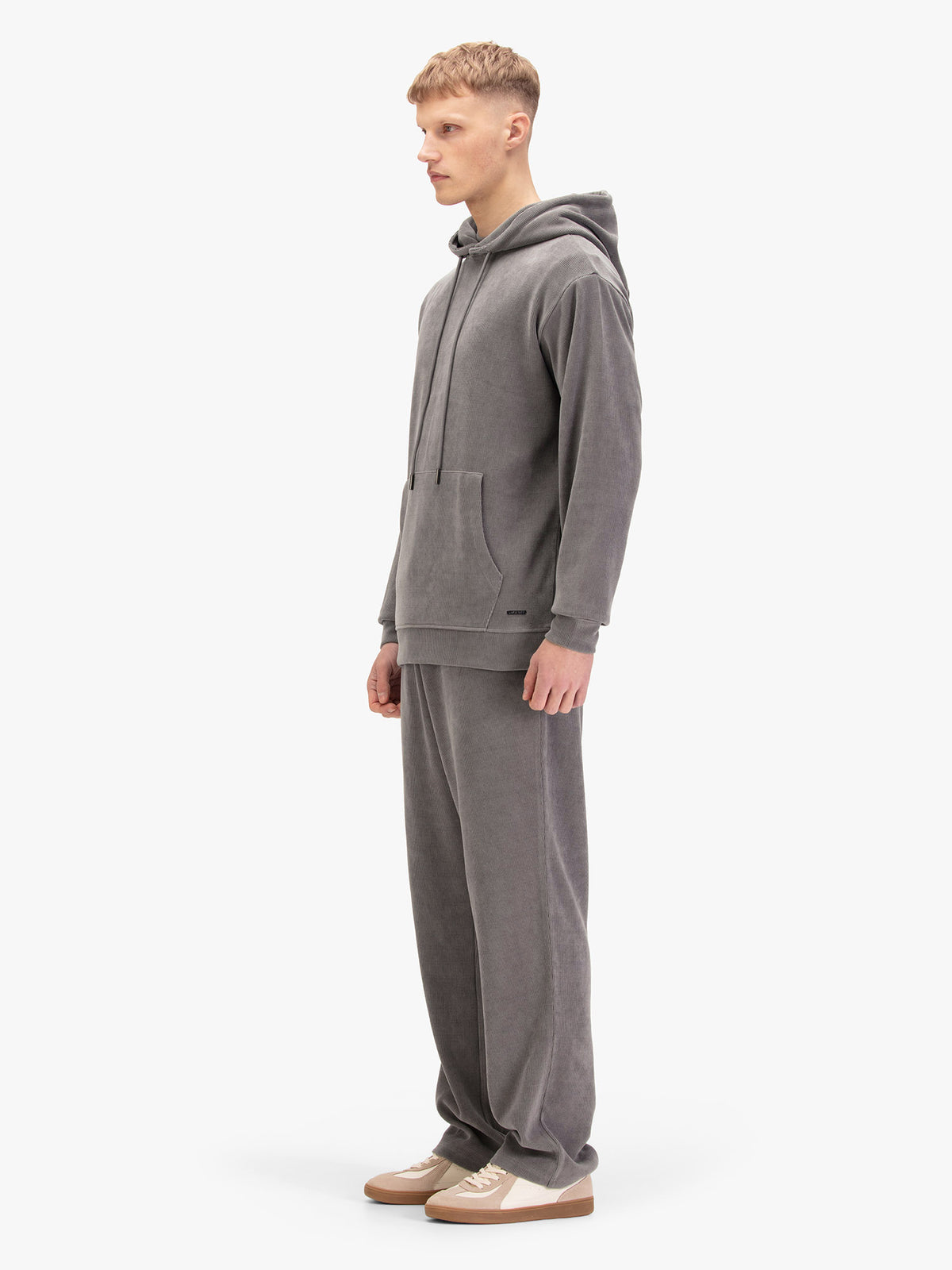 Men's relaxed-fit grey tracksuit with pullover hoodie and matching joggers, worn by a model, side view.