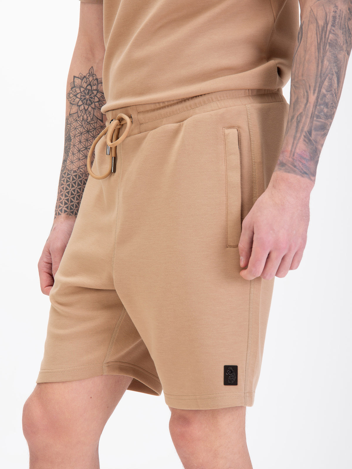 Men's beige shorts with drawstring waistband, worn by a model, detail view