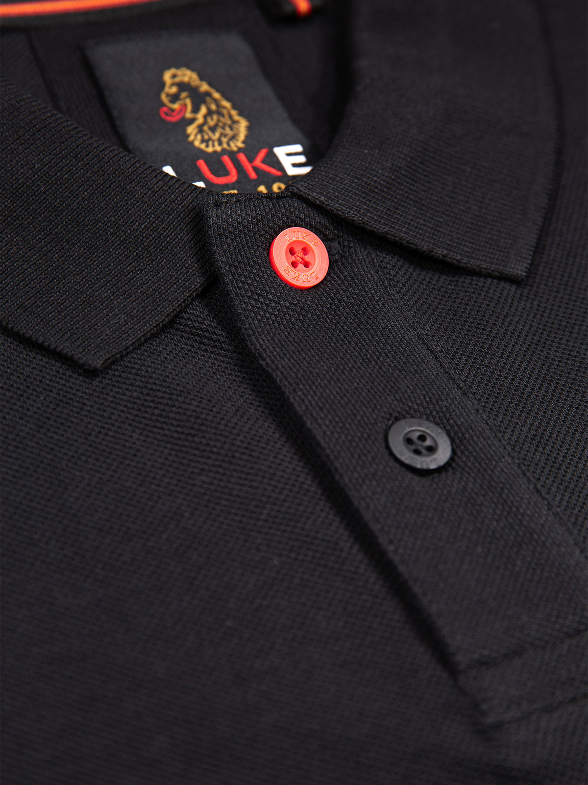 Close-up of marina red top button, smoke button and neck label on black New Mead polo shirt