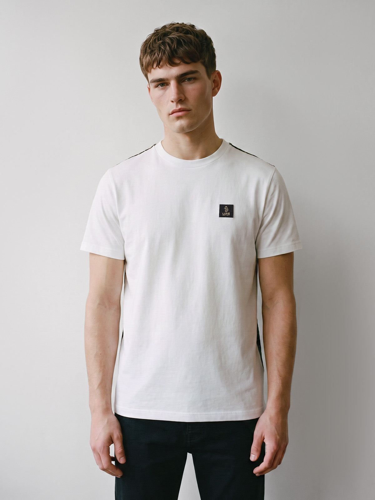 Man wearing white LUKE 1977 Burr t-shirt with black trousers, front view
