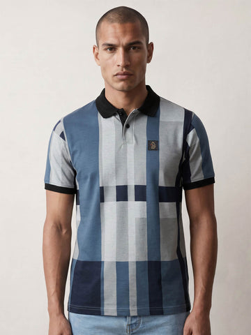 A man wearing a short-sleeve polo shirt with a blue, gray, and navy checkered pattern, black collar and sleeve cuffs, and a small embroidered logo on the chest, set against a plain light background.